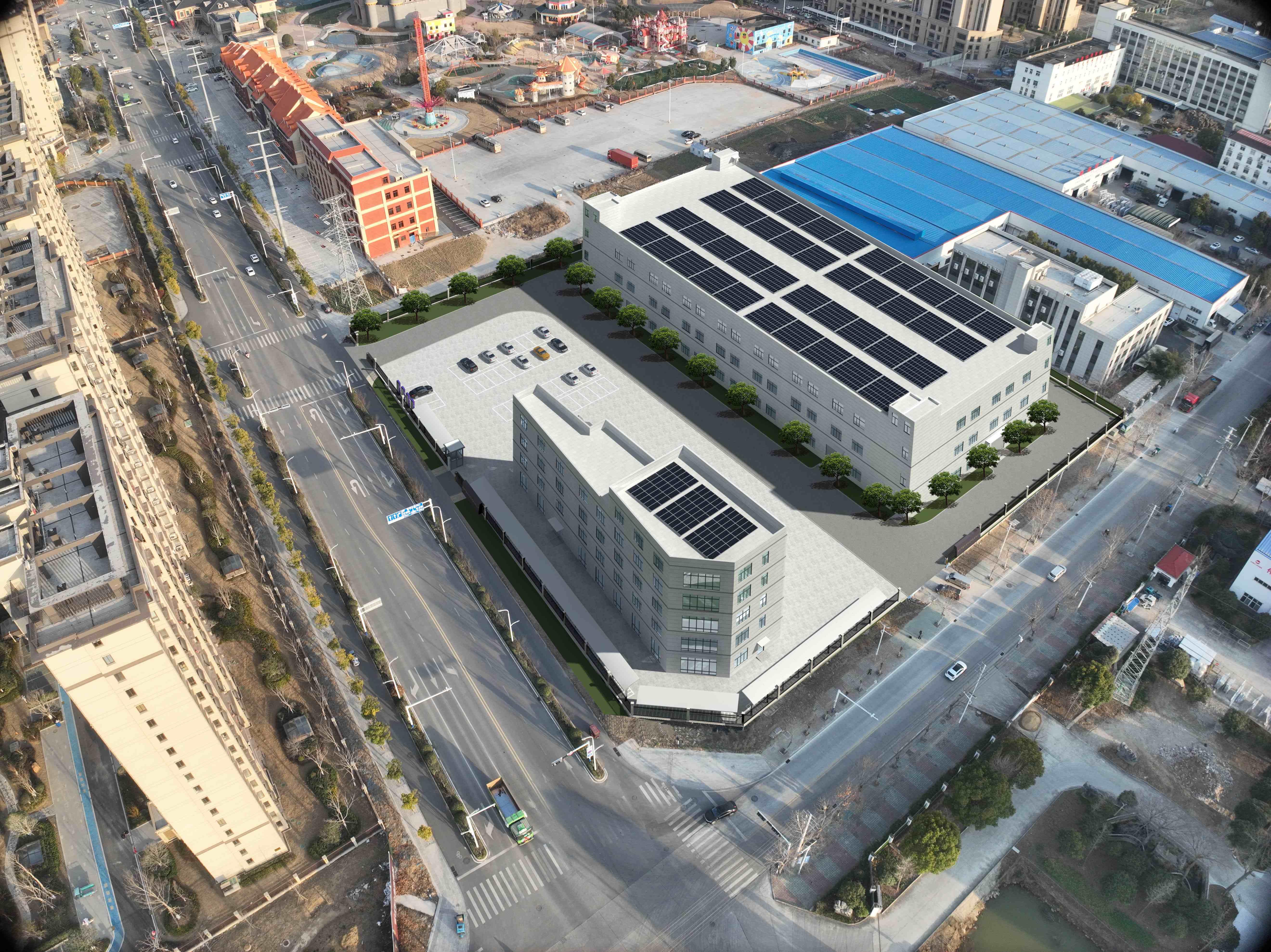 Aerial view of a modern factory building surrounded by greenery and a nearby road.